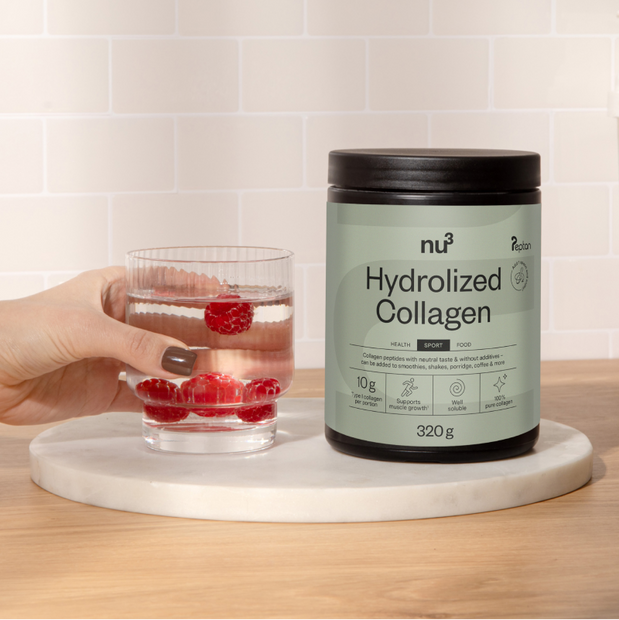 Collagendose auf Mamorplatte mit einem Glas Wasser mit Himbeeren